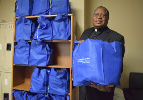 Father Deusdedit Byomuhangi, manager of pastoral care at OSF HealthCare Sacred Heart Medical Center in Danville, holds one of the bags ready for distribution to a needy family through the St. Nick's Closet program, a collaboration between Catholic Charities and OSF HealthCare. (The Catholic Post/Tom Dermody)